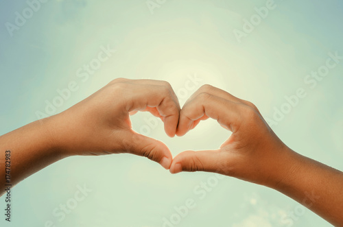 Heart shaped hands with noon sun and sky instagram tone