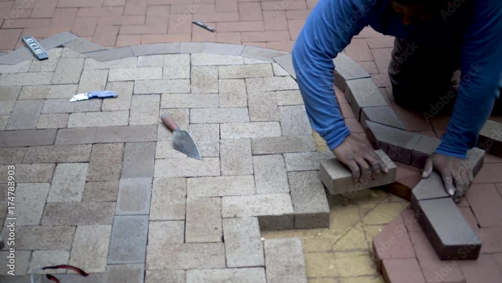 Steadicam shot of stone mason fitting and marking brick pavers for cutting for a two-tone emblem design integrating a herringbone pattern. Steadicam shot of stone mason fitting and marking brick pavers for cutting for a two-tone emblem design integrating a herringbone pattern.