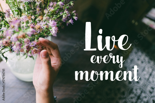 Life quote. Motivation quote on soft background. The hand touching purple flowers. Live every moment. photo