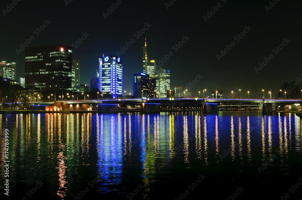 View of the Frankfurt skyline with blue-lit Union Investment building, the yellow-lit Commerzbank tower, IG Metall headquarters, life at front, and Friedensbruecke, from the south-west bank of the Main river at night, Frankfurt am Main, Hesse, Germany, Europe