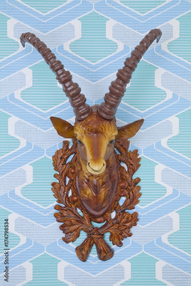 Fototapeta premium Plastic head of an ibex mounted on kitschy wallpaper from the 1960s or 1970s, frontal view