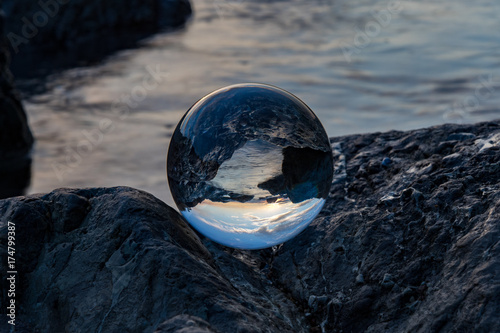 Glass ball on rocks looking at the ocean in the early morning light © Sheila