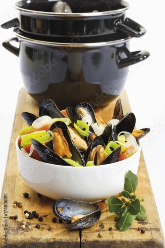 Mussels, rheinische art, with onions in a spicy sauce, in a porcelain dish in front of a mussel pot