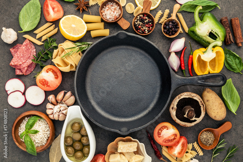 Italian food cooking ingredients on dark stone background with cast iron pan flat lay and copy space.