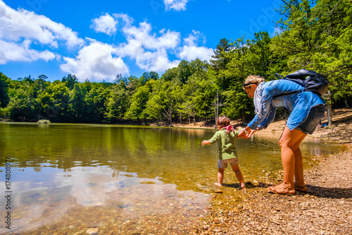 Tableau sur toile mother help baby to enter with feet in lake waters during a family trip in the n