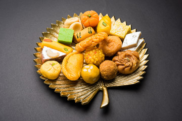 stock photo of Indian sweet or mithai and oil lamp or diya with gift box and flowers on decorative or colourful background, selective focus