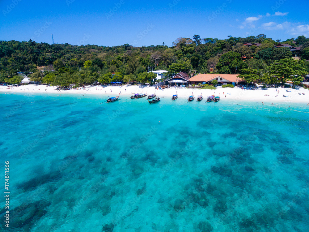 Fototapeta premium Aerial top view of tropical island with white beach and blue transparent water. Snorkeling people near wooden longtail boats above coral reef. Phi-Phi Don Island, Thailand.