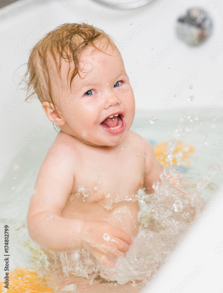 Laughing girl splashing in the water in the bathtub and looking at camera Laughing girl splashing in the water in the bathtub and looking at camera