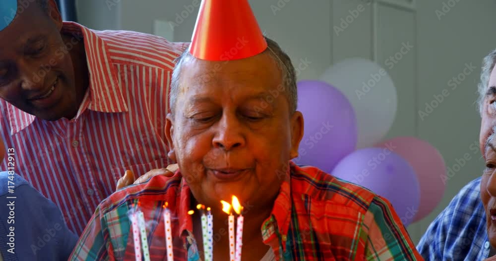 Senior man blowing out the candles on a birthday cake with his friends 