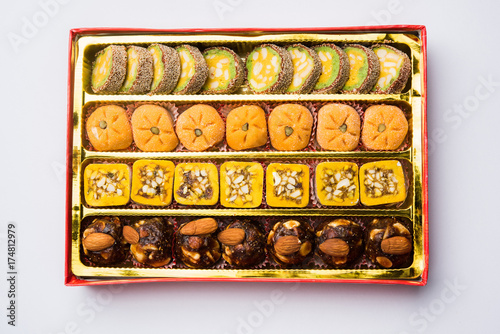 stock photo of Indian sweet or mithai and oil lamp or diya with gift box and flowers on decorative or colourful background, selective focus photo