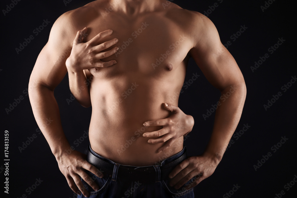 Foto de Female hands touching body of sporty young man on dark background  do Stock