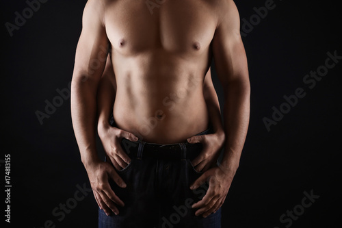 Female hands touching body of sporty young man on dark background