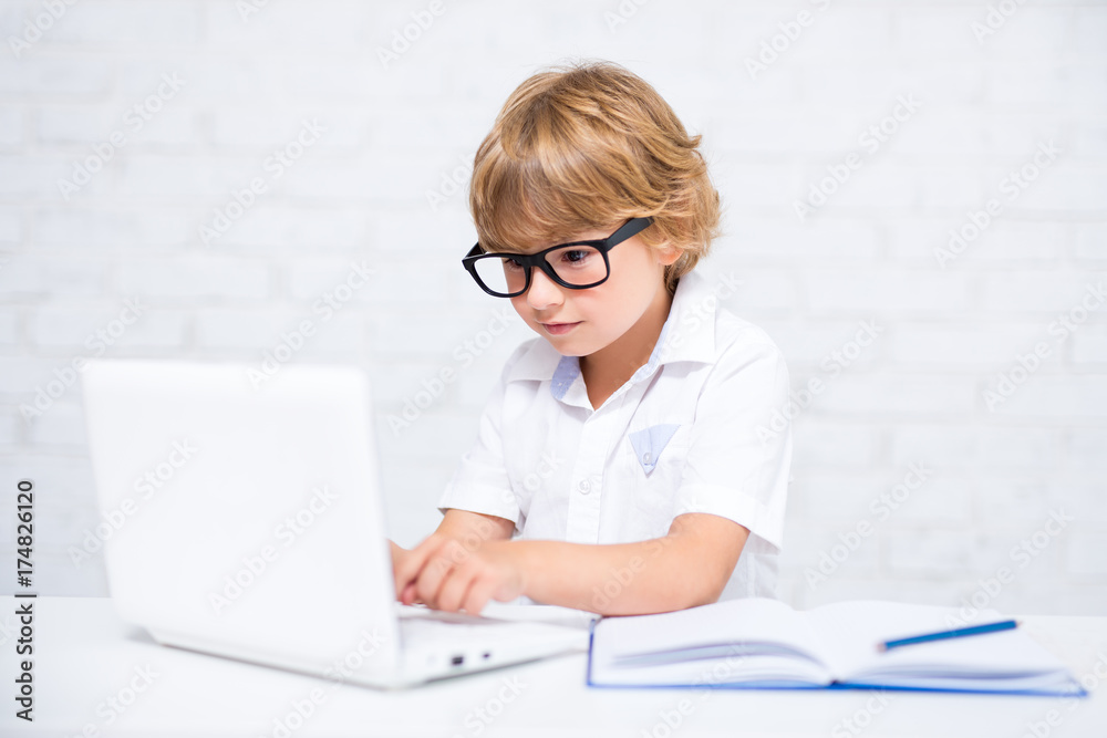 cute little school boy in glasses doing homework and using laptop cute little school boy in glasses doing homework and using laptop
