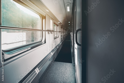 Wide-angle shooting of long and empty double-decker passenger train interior with multiple closed doors of compartments, hills outside the windows, carpet on the floor, railings on the walls