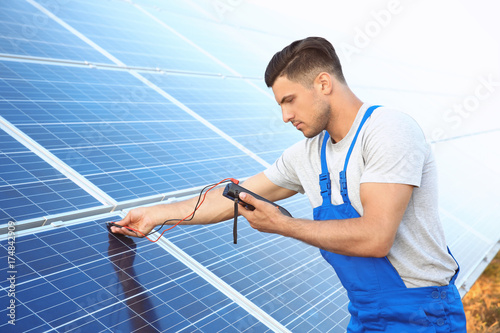 Young worker checking installation of solar panels by using multimeter