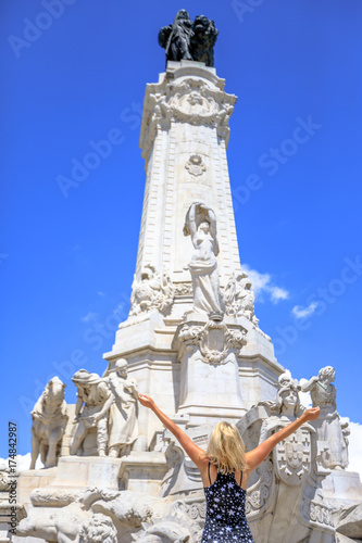 Happy tourist woman with open arms looking Marquess of Pombal Statue in Avenida da Liberdade in Lisbon, Portugal. Blonde caucasian female enjoying in Portuguese capital. Travel and Tourism in Europe.