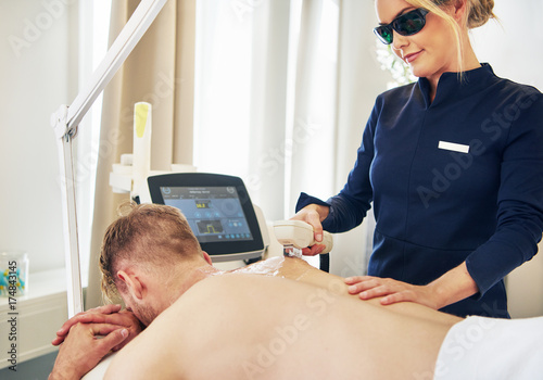 Young beauty technician performing laser hair removal on a client