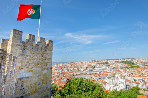 Lisbon aerial cityscape from Sao Jorge Castle on highest hill in Alfama. Waving portuguese flag on top of Lisbon Castle a popular tourist attraction. Panoramic view skyline of downtown on Tagus River.