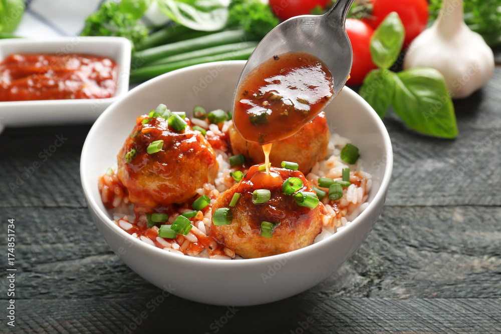 Pouring sauce onto delicious meatballs and rice in bowl on table Pouring sauce onto delicious meatballs and rice in bowl on table