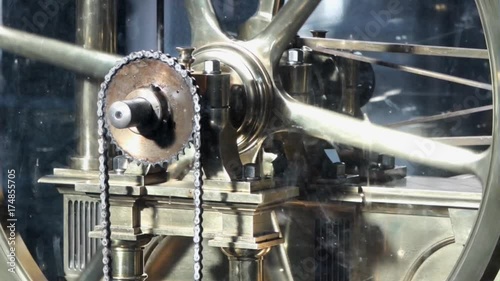 An old brass industrial beam engine wheel spinning with a chain.