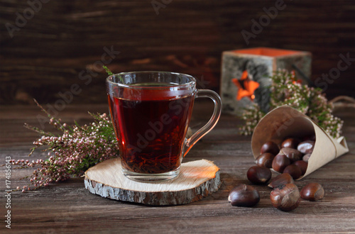 still life with a cup of tea, a bag of chestnuts, candle and heather on a dark wooden background