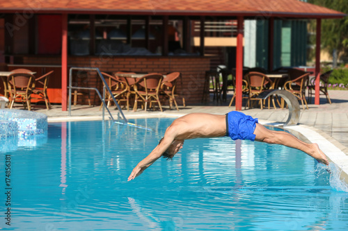 Young man jumping in swimming pool at resort
