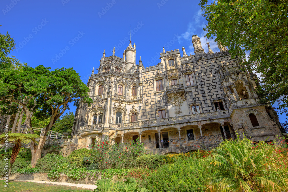 Gothic facade of grand house and gardens of mysterious Regaleira Palace or Monteiro Palace, landmark and Unesco Heritage in Sintra historic center, Portugal. Sunny day, blue sky.