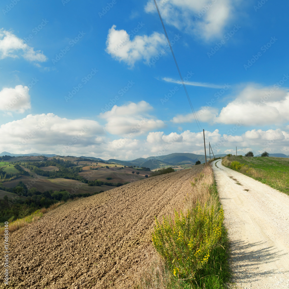 Panoramic view of a rural landscape with plowed fields and white country road