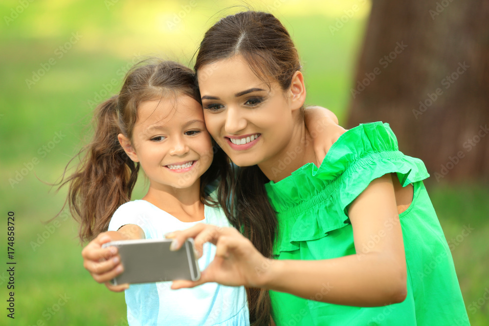 Cute little girl and mother taking selfie in park on sunny day Cute little girl and mother taking selfie in park on sunny day