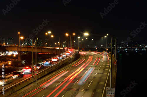 A view of The Gangbyeon Expressway, the road of Seoul at night. Four lane roads and ramps next to Han River. There are cars to work.