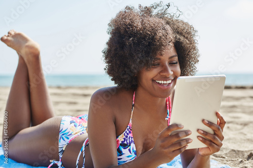 Happy afro american woman using tablet on beach