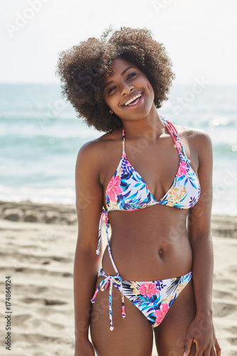 Young afro american woman in bikini standing on beach laughing