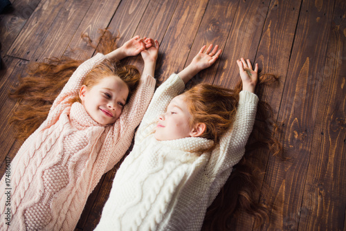 twin sisters in knitted sweaters lying on the floor