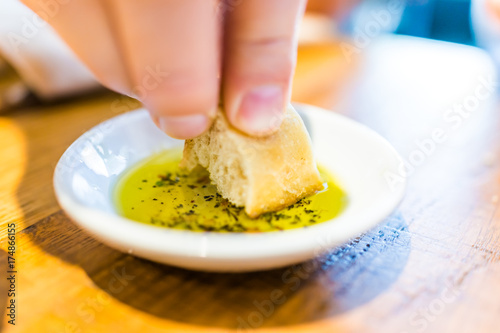 Photography Person's hand dipping slice of bread in herbed olive oil in restaurant