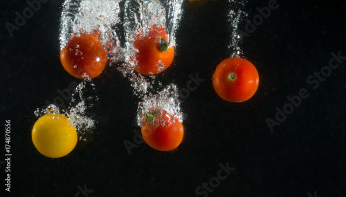 Ripe red and yellow tomato in splashes of water on a black background.