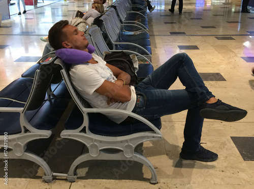 A young guy is sleeping on a chair at the airport, putting a pillow under his head,