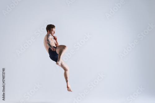 Freeze action portrait of shirtless young Caucasian sportsman or boxer in trunks in the middle of spacious studio jumping with focused look during work out. Endurance, speed and power concept