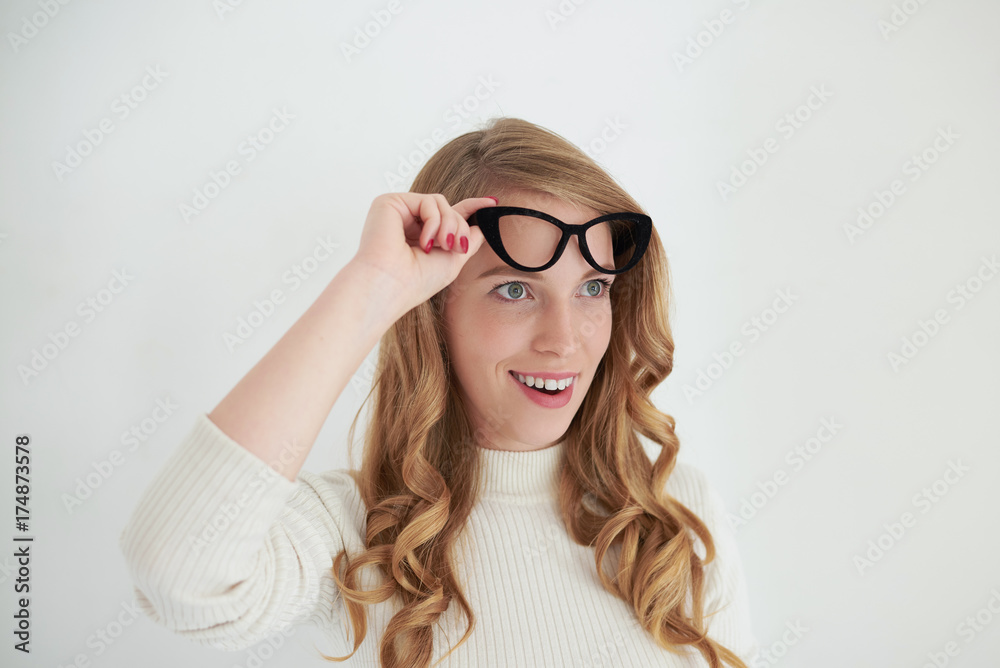 Horizontal shot of fascinated or astonished young European female wearing turtle neck holding stylish eyeglasses at her head and looking ahead of her with amazed shocked expression. Human emotions