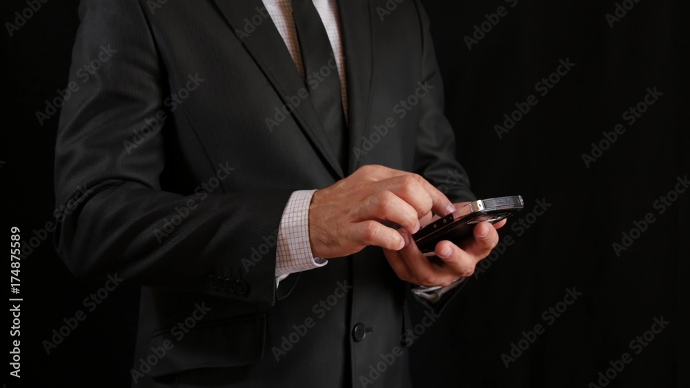 Concept, digital online life and social networks. A businessman in a black business suit with a tie uses his smartphone to view his accounts. Concept, digital online life and social networks. A businessman in a black business suit with a tie uses his smartphone to view his accounts.
