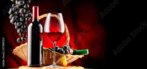 Wine. Bottle and glass of red wine with ripe grapes over black background