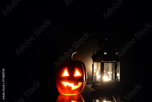 Тыква с вырезанными глазками и ртом, со свечой внутри, на темном фоне рядом с фонарем - символом Хеллоуин

