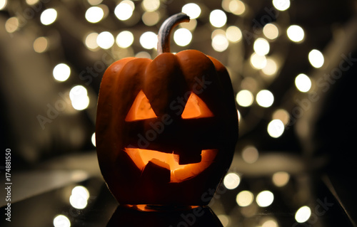 Тыква с вырезанными глазками и ртом, со свечой внутри, на темном фоне рядом с фонарем - символом Хеллоуин

