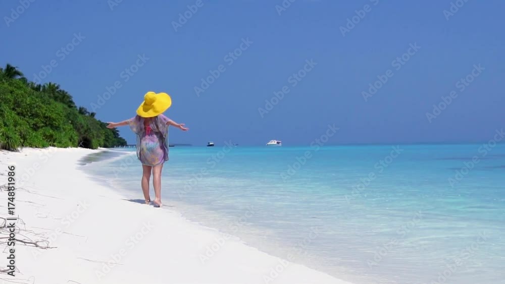 Woman in straw yellow sunhat walking along the beach with turquoise sea water Woman in straw yellow sunhat walking along the beach with turquoise sea water