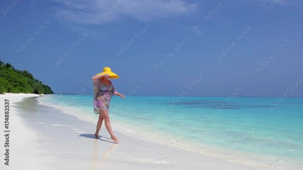Woman in straw yellow sunhat walking along the beach with turquoise sea water Woman in straw yellow sunhat walking along the beach with turquoise sea water