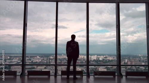 Rear view of businessman in an office with panoramic city view. Businessman admires the city from the panoramic Windows in the city centre