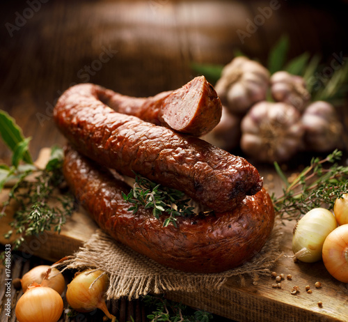 Smoked  sausage on a wooden rustic table with addition of fresh aromatic herbs and spices, natural product from organic farm, produced by traditional methods