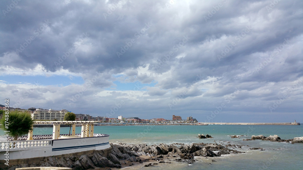 view of the sea shore against the backdrop of the city center on a sunny day. Storm clouds in the sky. Castro-Urdiales, Cantabria, North Spain.