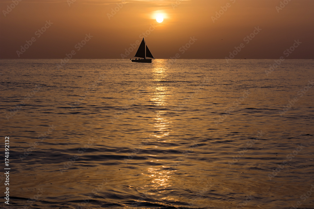 sail boat silhouette on the horizon just after sunrise