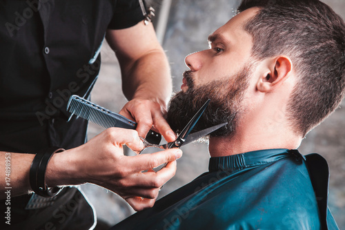 Handsome bearded man having his beard cut by hairdresser at the barbershop. A professional job with a dangerous razor, salon