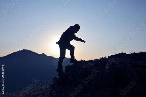 silhouette of a man who climbs the mountain on a background of dawn.